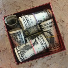 several rolls of one hundred dollar bills in a red box on a marble counter top