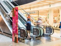 people are moving down an escalator in a shopping mall with signs on them