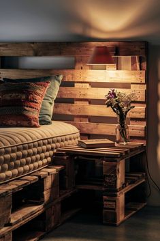 a bed made out of pallet wood with a lamp on the side and flowers in a vase