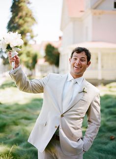 a man in a suit and tie holding flowers up to the camera with his hand