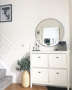 a white dresser with a round mirror above it and a potted plant next to it