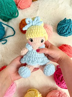 a person holding a small crocheted doll next to balls of yarn