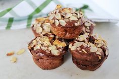 four chocolate muffins with almonds on top sitting on a white surface next to a green and white napkin