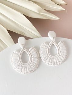 two pairs of white earrings sitting on top of a table next to a palm leaf