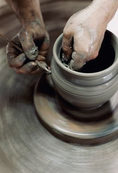 a person working on a potter's wheel with one hand and the other holding a tool