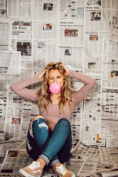 a woman sitting on the floor with a bubble in her mouth and newspapers behind her