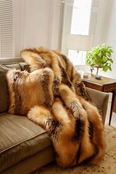 a couch with some fur on it in front of a window and a potted plant