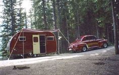 an old red truck parked in front of a trailer home next to a tree filled forest