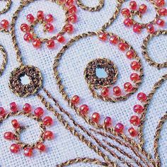 some red beads and chains are laying on a tablecloth with white fabric in the background