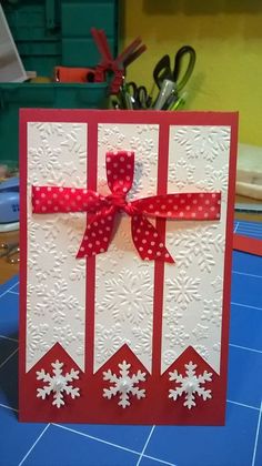 a handmade christmas card with red ribbon and snowflakes on it, sitting on a table