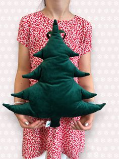 a woman holding a green christmas tree pillow in her hands and wearing a red dress