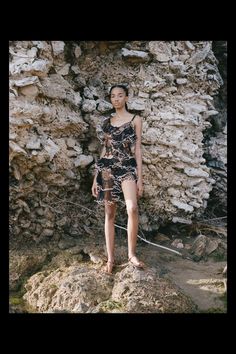 a young woman standing on top of a rock next to a stone wall and holding a rope