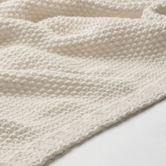 a white knitted blanket laying on top of a bed