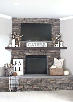 a living room with a stone fireplace and tv above the mantle is decorated for fall