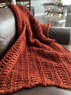 an orange crocheted blanket sitting on top of a brown leather couch in a living room