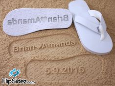 two pairs of white flip flops are on the sand, one is personalized