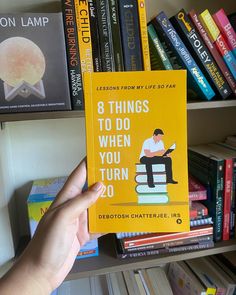 a person holding up a yellow book in front of a bookshelf full of books