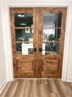 two wooden doors with glass panels in an empty room and wood flooring on the other side