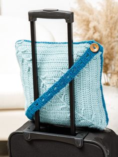 a blue crocheted bag sitting on top of a black suitcase next to a white couch