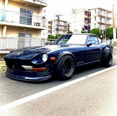 a blue sports car is parked on the side of the road in front of apartment buildings