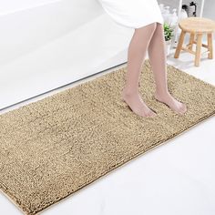 a woman standing on top of a bath mat next to a white tub and wooden stool