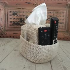 a crocheted basket with remote controls and tissue in it