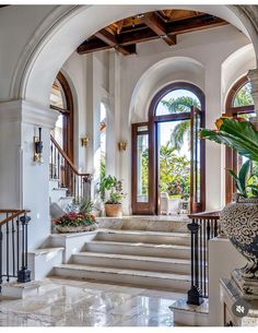 an entry way with stairs, potted plants and large windows on either side of the door