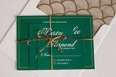 a green and gold wedding card with a bow tied around the front, on top of a white envelope