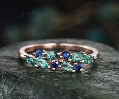 a ring with blue and green stones sitting on top of a stone slab in front of a dark background