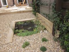 a small pond in the middle of a graveled area next to a brick building