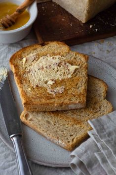 two pieces of bread on a plate with butter and honey in the bowl next to it