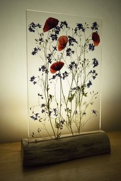 a glass vase with flowers in it sitting on a wooden table next to a light