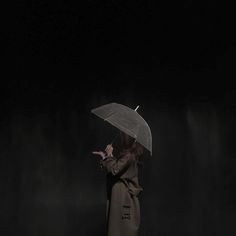 a woman standing in the dark holding an umbrella over her head and pointing at something