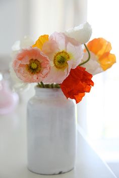 a white vase filled with colorful flowers on top of a table