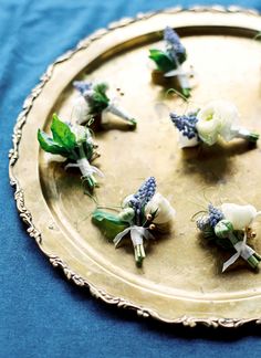 small white flowers are placed on a gold tray with blue fabric behind it and green leaves in the middle