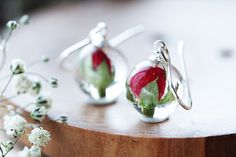 two red and green earrings sitting on top of a wooden table next to white flowers