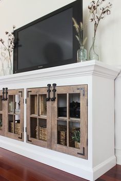 an entertainment center with glass doors and baskets on the bottom, in front of a flat screen tv