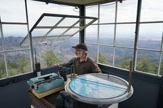 a man sitting at a table in front of a window looking out on the mountains