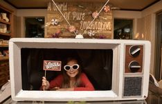 a woman wearing sunglasses and holding a sign in front of a microwave with the door open