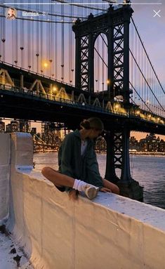 a man sitting on top of a wall next to a bridge