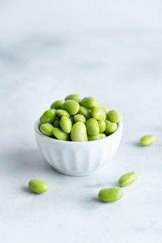 a white bowl filled with green beans on top of a table next to some nuts