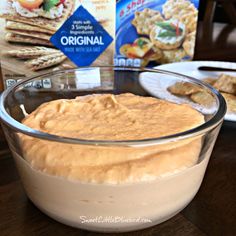 a glass bowl filled with hummus and crackers next to a box of crackers