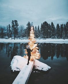 a man standing on a dock next to a lit christmas tree in the middle of a lake