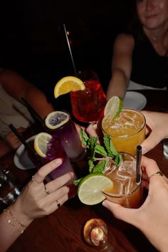 several people are sitting at a wooden table with drinks in front of them and holding their hands together