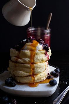 a stack of pancakes with syrup being drizzled over them on a plate