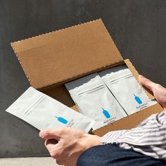 a person is holding two bags of tea in front of a box with the same bag on it