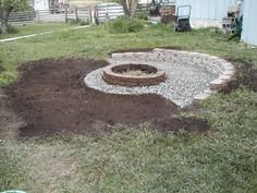 a fire pit in the middle of a yard with gravel around it and grass surrounding it