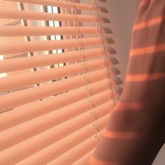 a person's hand is holding the blinds in front of their face and arm