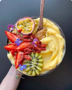 a person holding up a bowl with fruit on it and a spoon in the bowl