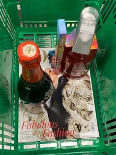 a green shopping basket filled with bottles of wine and condiments on top of a magazine